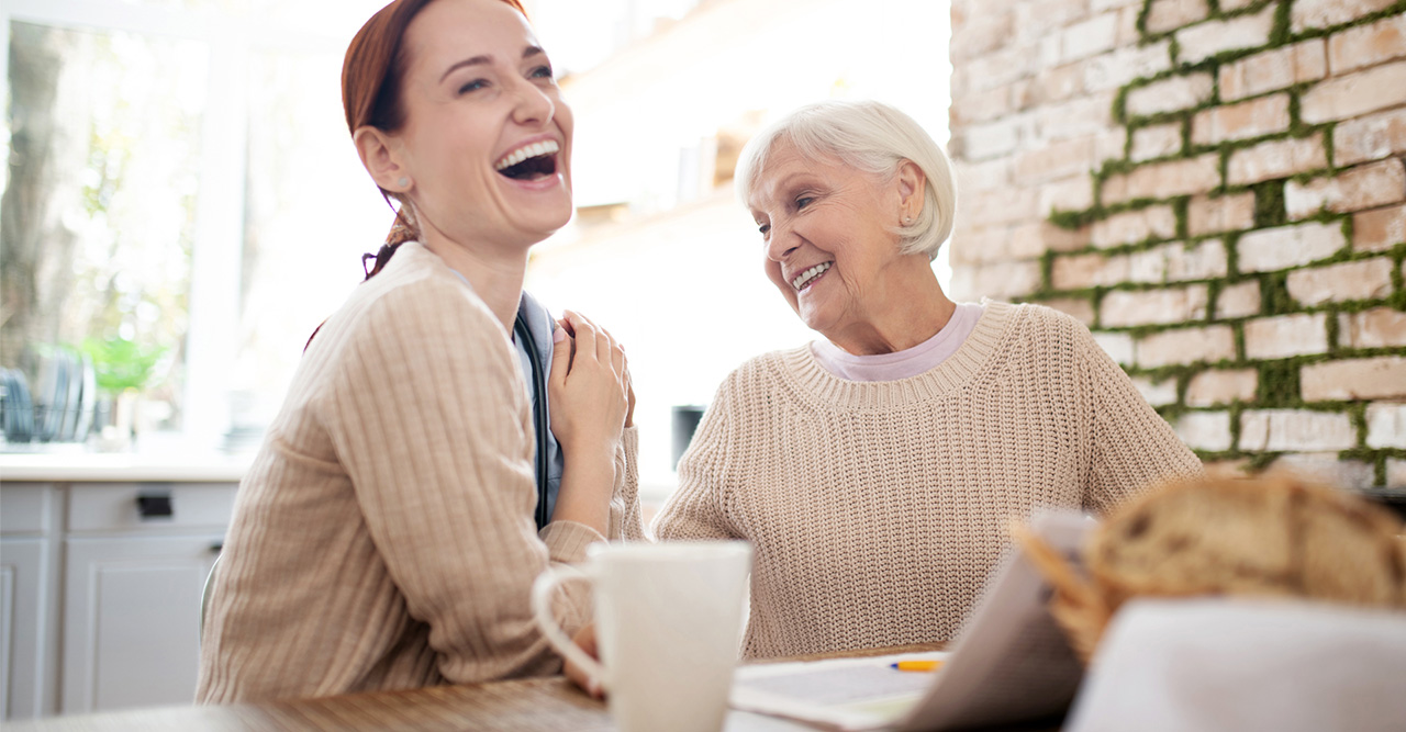 red haired caregiver laughing while pensioner joking